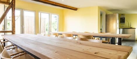 Una habitación amplia con una larga mesa de madera y sillas, una escalera y una zona de cocina.
