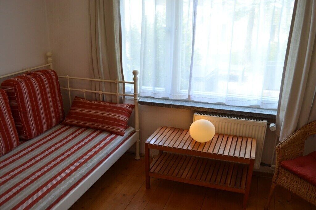 A room with a bed, a small table with a lamp, and a window with curtains.