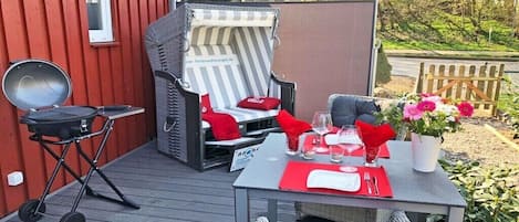 Une terrasse avec un barbecue, une chaise dotée d’un coussin à rayures, une table dressée pour le repas et une chaise en osier avec des coussins.