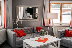 Ein Wohnzimmer mit grauem Sofa, roten Kissen, einem weißen Couchtisch, einem Spiegel und einer Stehlampe.