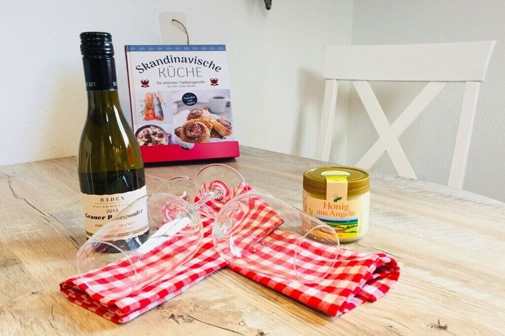 Une bouteille de vin, une boîte de pâtisseries, un pot de miel et un tissu à carreaux rouges et blancs sur une table en bois.