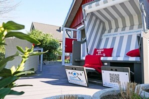 A covered outdoor seating area with a striped awning, a red pillow, and a QR code sign. - Holiday home with 1 bedroom (Grödersby)