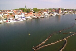 A river with a boat docked on the left, a bridge in the background, and buildings along the riverbank. - Holiday home with 1 bedroom (Grödersby)