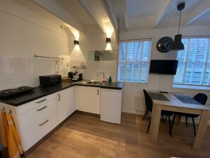 A modern kitchen with white cabinetry, a black countertop, and a dining area with a table and chairs. - Holiday Apartment With 1 Bedroom (Schoorl)