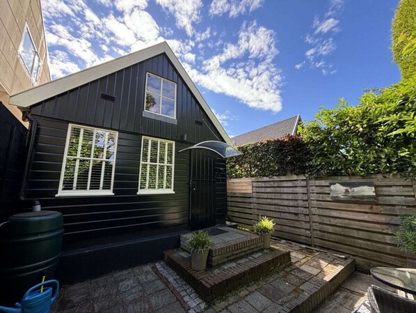 A black house with a sloped roof, a small porch with steps, and a wooden fence. - Holiday Apartment With 1 Bedroom (Schoorl)