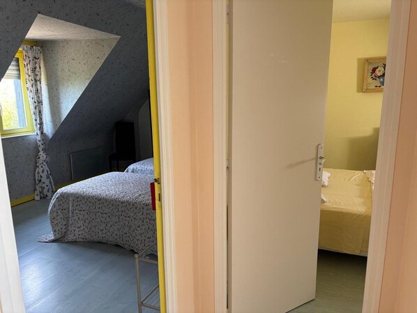 A bedroom with a bed, a chair, a radiator, and a window with curtains. - Normandy Gite With Bay Views (Courtils)