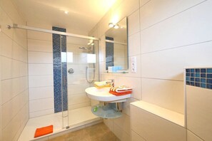 Een moderne badkamer met een douchecabine van glas, een witte wastafel met spiegel erboven en een betegelde vloer.