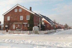 A brick building with a white picket fence, a sign reading 'Hans Seester,' and a visible storefront with a sign that says 'Hansen Seester.' - Seestern 5 Apartment House Seestern (Norderney)
