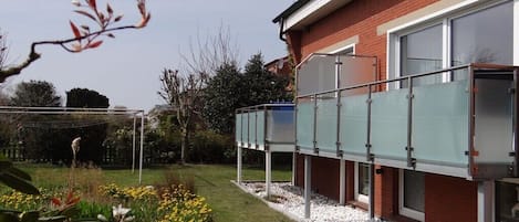 Ein Wohngebäude mit Glasfassade und Backsteinfassade, sowie ein Garten mit gelben Blumen.