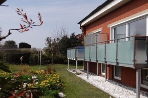 A residential building with a glass enclosure, a brick facade, and a garden with yellow flowers. - Seestern 7 Apartment House Seestern (Norderney)