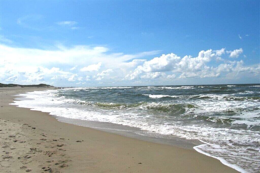 A beach with waves, a clear sky, and a distant shoreline.