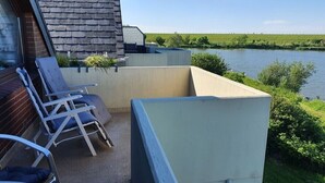 Un balcon donnant sur une rivière, un mur de briques et deux fauteuils de relaxation.