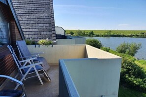 A balcony with a view of a river, a brick wall, and two lounge chairs. - Holiday apartment with 1 bedroom (Nordstrand)