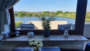 Une pièce avec vue sur un lac, une plante en pot, un vase de fleurs et une radio posée sur une table.