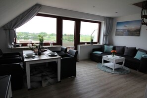 A modern living room with a dining area, large windows, and a view of the outdoors. - Holiday apartment with 1 bedroom (Nordstrand)