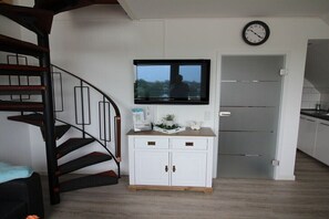 Een trap met een zwarte leuning, een wit kastje met lades, een flatscreen televisie die erboven is bevestigd, en een klok aan de muur.