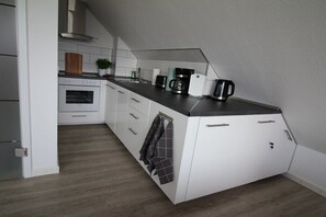 Een compacte keuken met witte kastjes, een inbouwoven, een koffiezetapparaat en een waterkoker op het aanrecht.