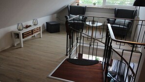 Un salon moderne avec un escalier, un coin salon comprenant deux fauteuils, une petite table et une console blanche agrémentée d’objets décoratifs.