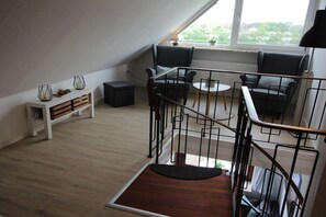 Ein modernes Wohnzimmer mit Treppe, einer Sitzecke mit zwei Sesseln, einem kleinen Tisch und einem weißen Konsolentisch mit Dekoration.