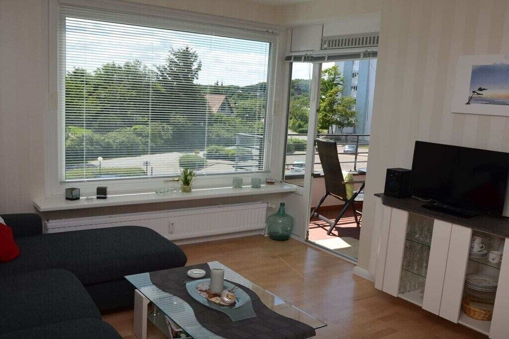 Een woonkamer met een bank, een salontafel, een televisie en een groot raam met jaloezieën.