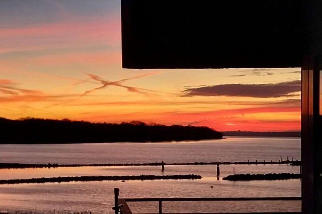 Vista al atardecer desde un balcón con barandilla, un cuerpo de agua y una costa lejana.