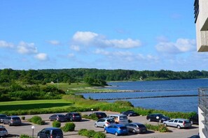 A parking area with cars, a body of water, and greenery in the background. - Holiday apartment with 1 bedroom (Glücksburg)