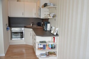 A compact kitchen with a built-in oven, a coffee maker, and a bookshelf filled with books. - Holiday apartment with 1 bedroom (Glücksburg)