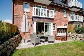 A two-story brick house with a balcony, a patio with outdoor furniture, and a stone wall. - Villa Jansen 5 - OG/DG (Wenningstedt)