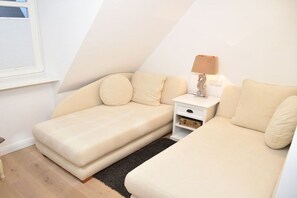 Ein kleiner, gemütlicher Raum mit zwei beigen Sofas, einem weißen Nachttisch mit Lampe und einem Fenster.