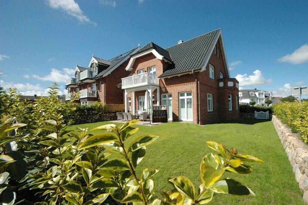Une maison à deux étages avec un balcon, une pelouse bien entretenue et un mur en pierre.