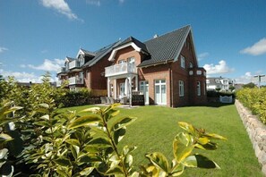A two-story house with a balcony, a well-maintained lawn, and a stone wall. - Villa Jansen 5 - OG/DG (Wenningstedt)