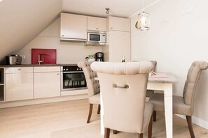 A modern kitchen with a dining area, featuring a microwave, oven, and a red appliance on the counter. - Villa Jansen 5 - OG/DG (Wenningstedt)