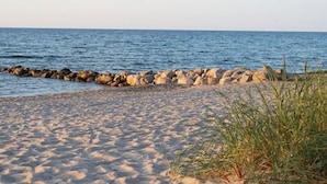 Une plage de sable avec une digue rocheuse et une eau d’un bleu limpide.