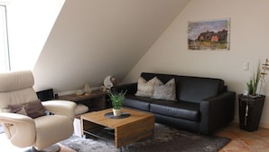 Un salon moderne avec un canapé en cuir noir, un fauteuil blanc et une table basse en bois.