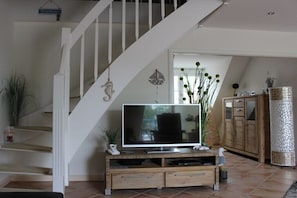 Un escalier avec une rampe blanche, un téléviseur à écran plat posé sur une console en bois et un meuble avec des tiroirs.
