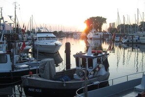 Un port de plaisance où sont amarrés différents types de bateaux, un coucher de soleil en arrière-plan et une eau calme qui reflète le paysage.