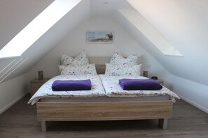 A bedroom with a sloped ceiling, a bed with floral bedding, two pillows, and a small bedside table. - Holiday apartment with 1 bedroom (Timmendorfer Strand - Niendorf)