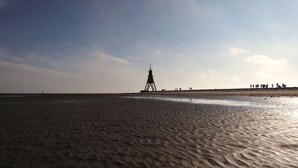 A sandy beach with a lighthouse in the distance and a group of people on the right. - Holiday apartment with 1 bedroom (Cuxhaven)