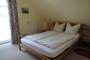 A single bed with a wooden frame, a radiator, a lamp, and a window with curtains. - Holiday apartment with 1 bedroom (Cuxhaven)