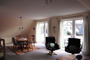 Une pièce comprenant une table à manger, des chaises, un fauteuil en cuir noir et une fenêtre avec des rideaux.