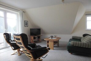 A living room with a television, two chairs, a small table, and a sofa. - Holiday apartment with 1 bedroom (Cuxhaven)