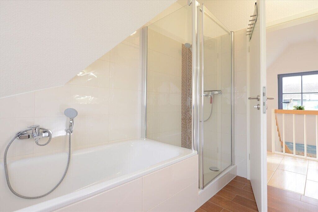 A modern bathroom with a glass-enclosed shower, a standalone bathtub, and a visible window.