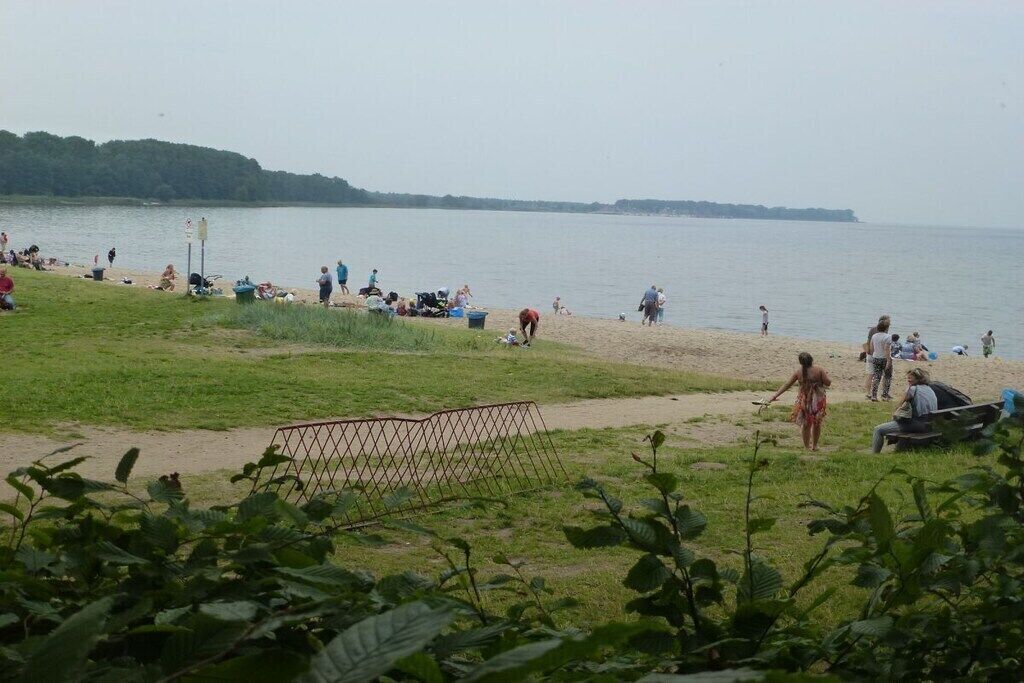Uma praia com pessoas, uma área gramada e um corpo de água.