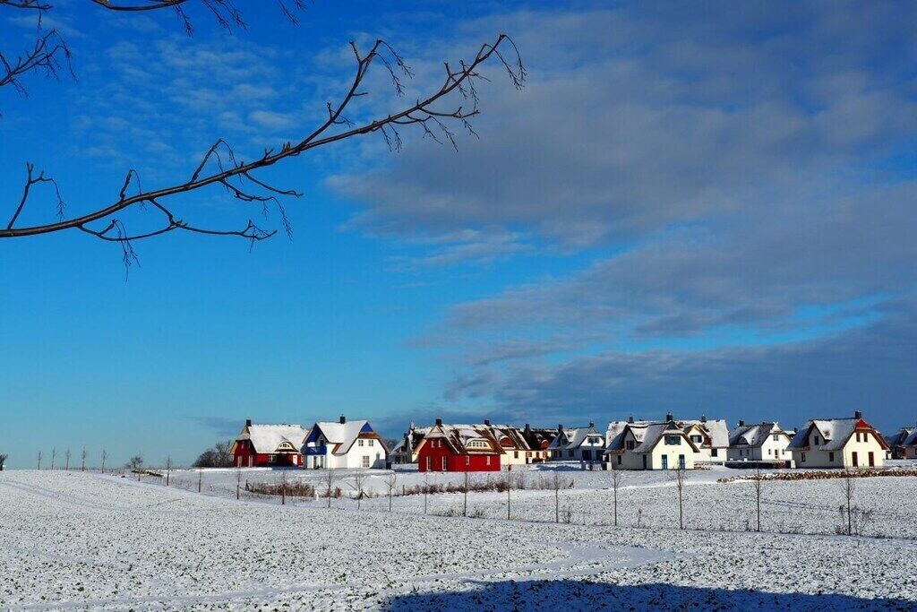 Ein verschneites Dorf mit traditionellen Häusern, einem klaren Himmel und einem mit Schnee bedeckten Feld.