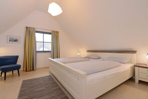 Ein Schlafzimmer mit einem Einzelbett, einem Nachttisch, einem Sessel und einem Fenster mit Vorhängen.