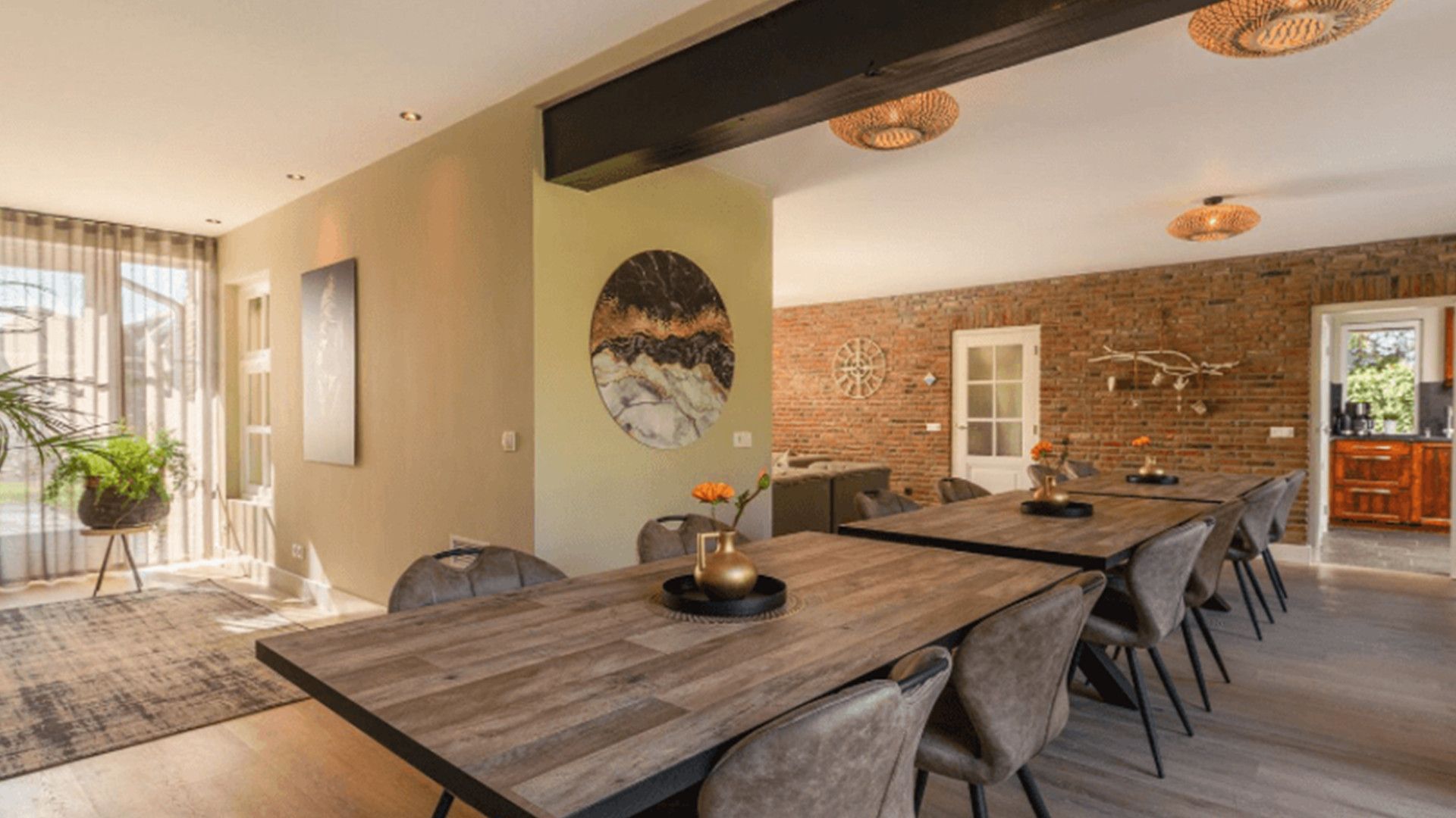 A modern dining area with a long wooden table, multiple chairs, and a brick wall.