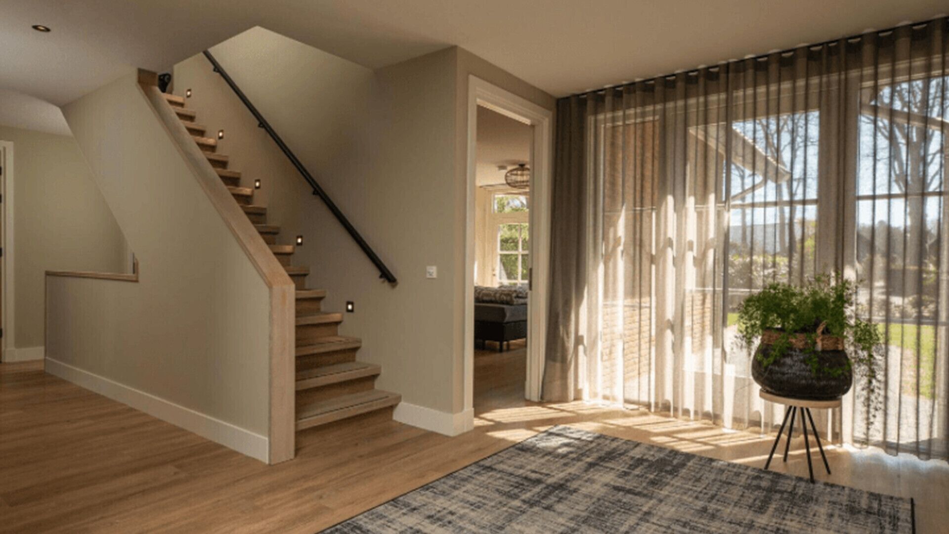 A staircase with wooden steps and a black handrail, leading to a room with a large window and a potted plant.