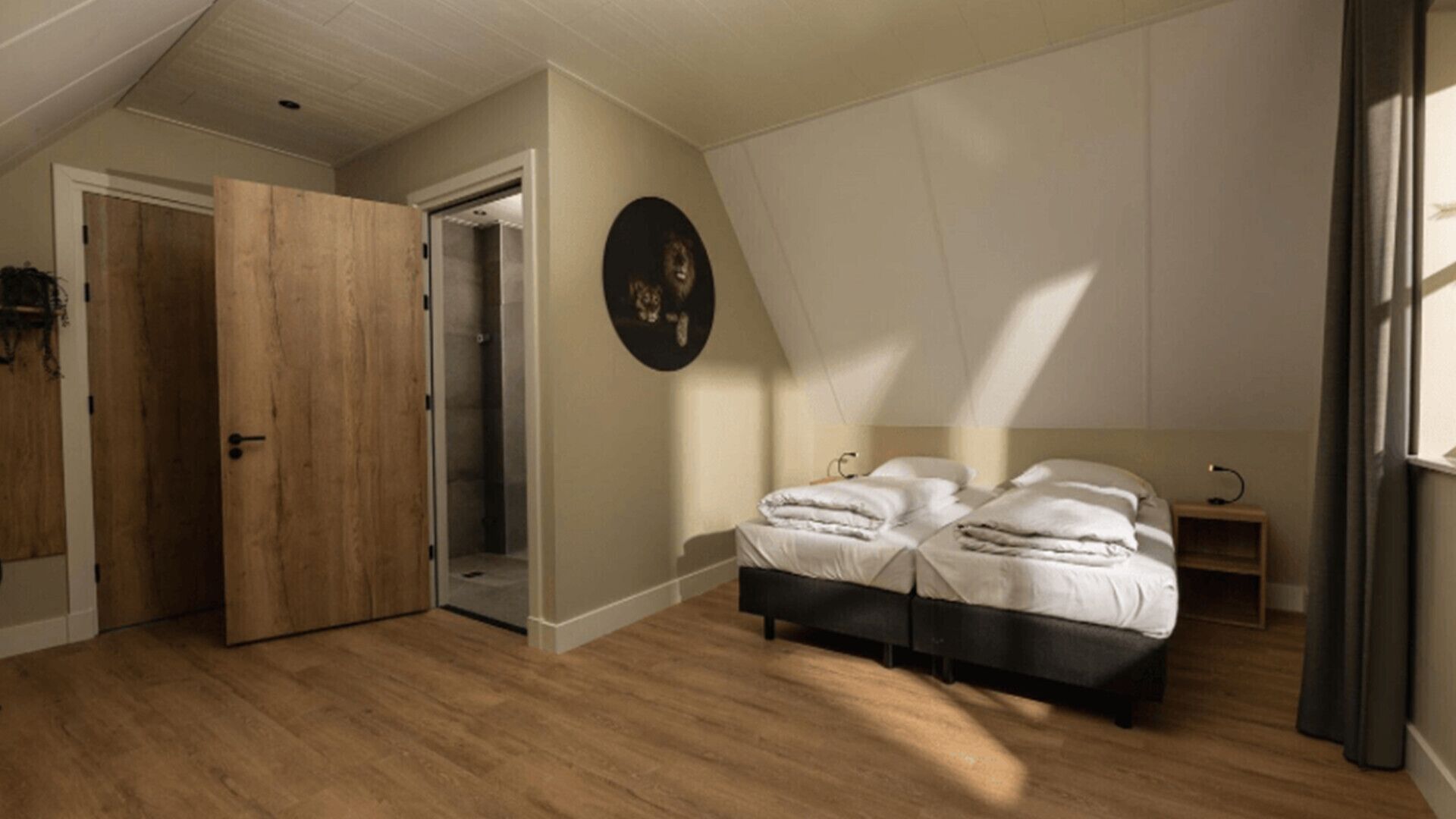 A bedroom with a wooden floor, a bed with white bedding, a small bedside table, and a door leading to a shower.