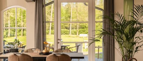An indoor dining area with a table and chairs, large windows, and a potted plant.