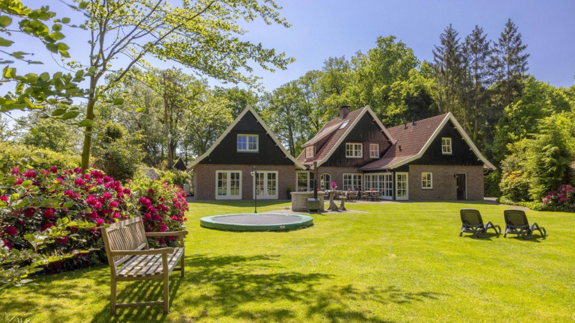Une maison à deux étages avec une pelouse bien entretenue, un espace extérieur aménagé pour s’asseoir et un jardin circulaire.